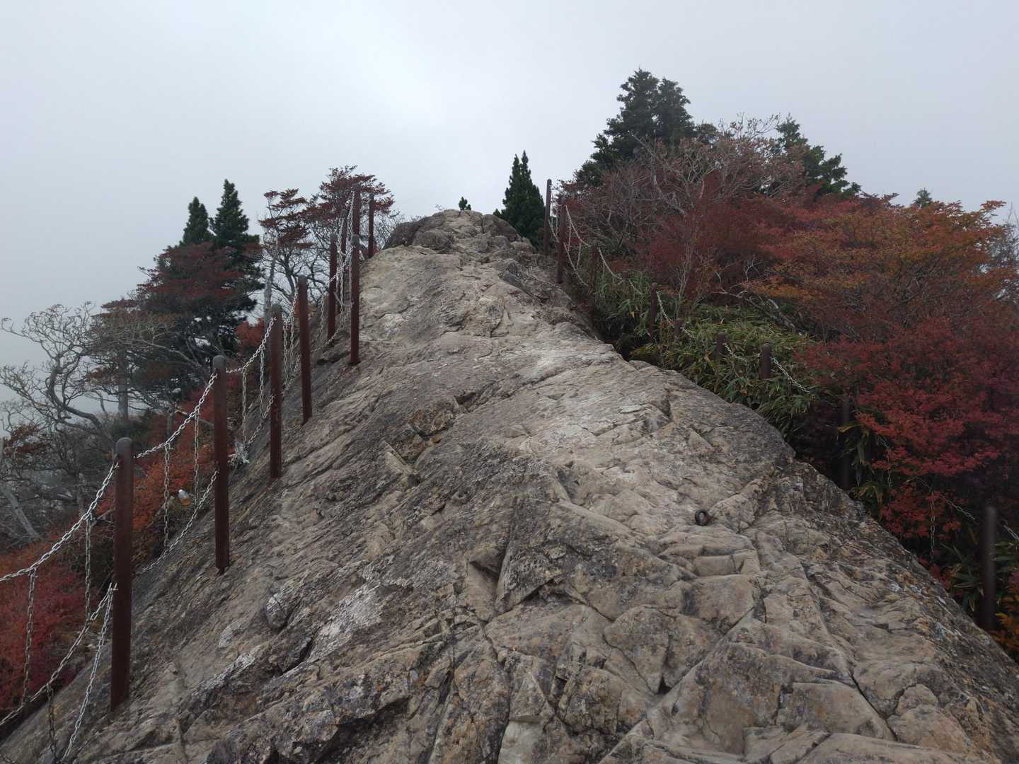 大蛇嵓の岩場と鎖の柵、その奥に広がる紅葉